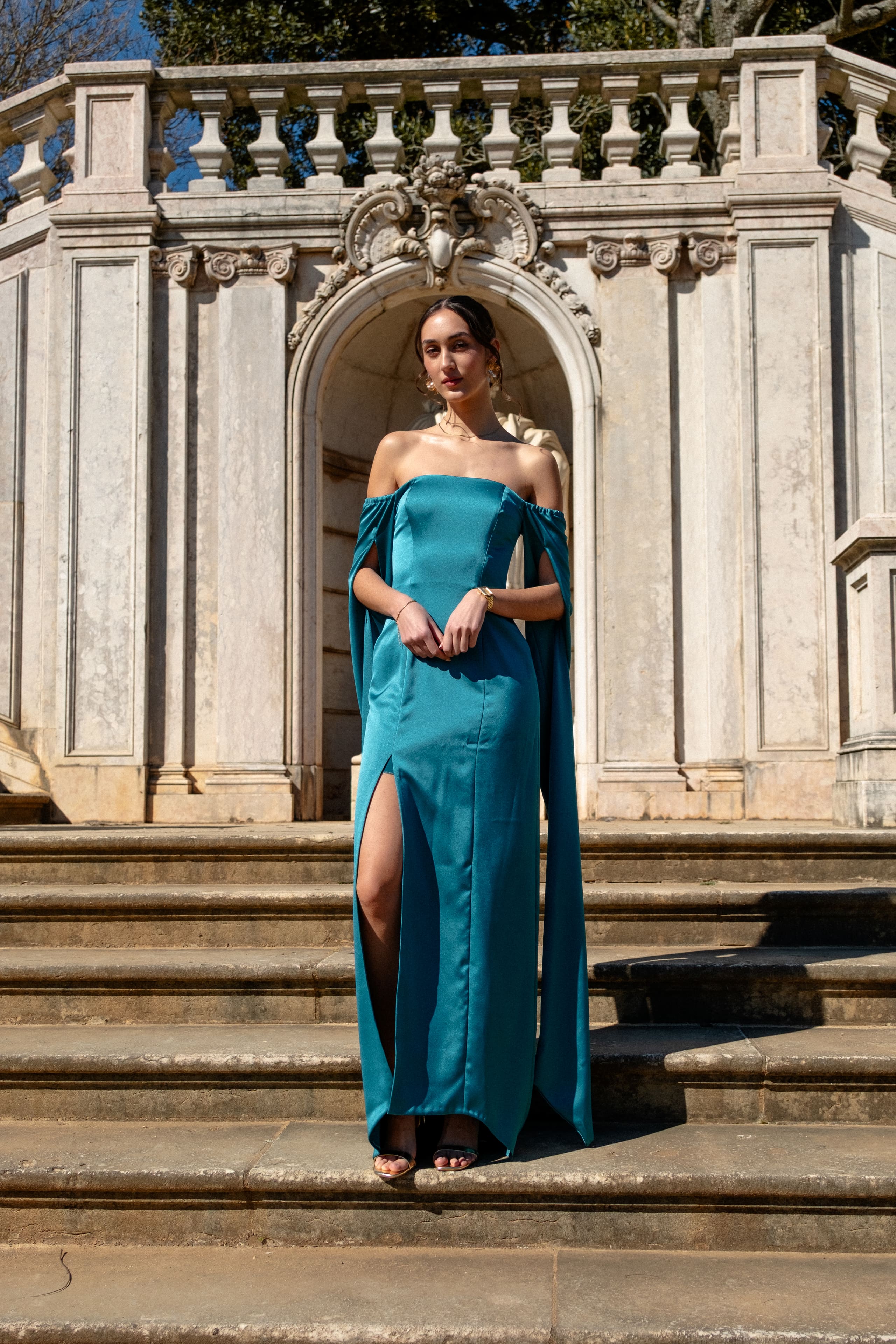 Mulher em vestido de cetim petróleo numa escadaria barroca